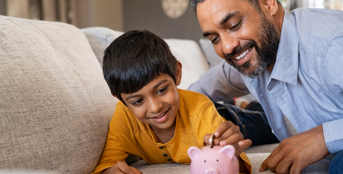 Father helping son put coins into piggy bank.